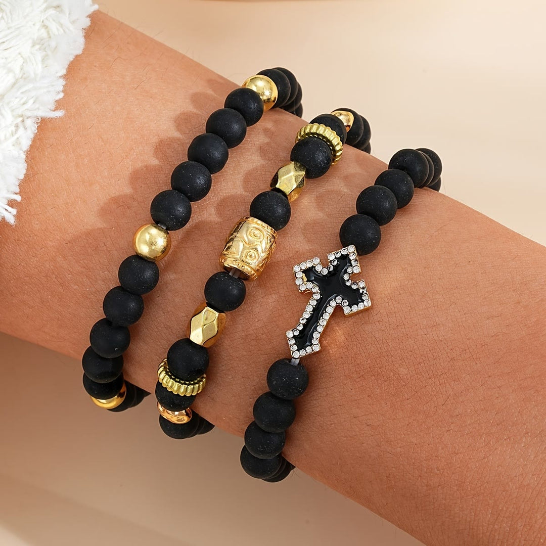 Christianartworkshop Mehrlagiges, dehnbares Armband aus mattschwarzen Steinperlen mit Zirkonia-Kreuz und gravierten Goldzwischenstücken - image 1